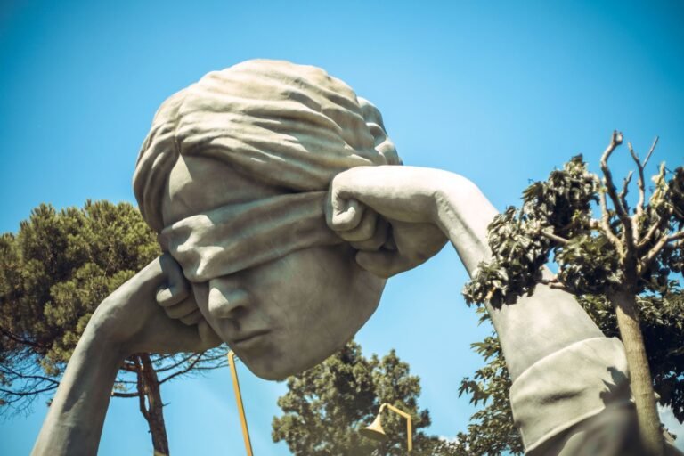 Proporcionalidade nas sanções administrativas: quando a punição do Estado é excessiva 3 Outdoor sculpture of a blindfolded head amid lush greenery on a clear day.