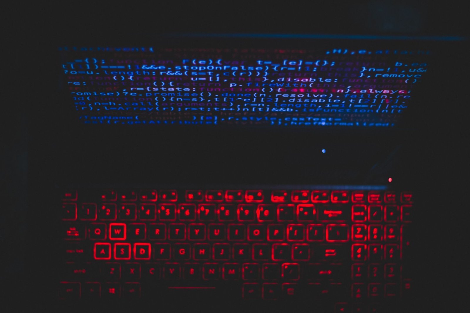 Dark-themed laptop setup with a red glowing keyboard and code on screen, ideal for tech en