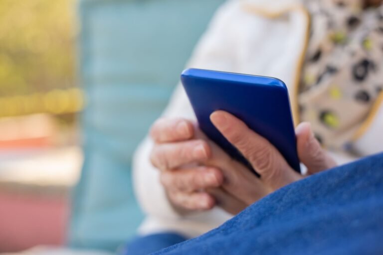 Senior adult using a smartphone outdoors on a sunny day. Focus on hands and device.