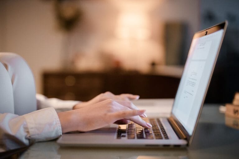 Prova digital em contratos: como guardar e-mails e mensagens com segurança 4 Close-up of hands typing on a laptop at home, showcasing a cozy work environment.