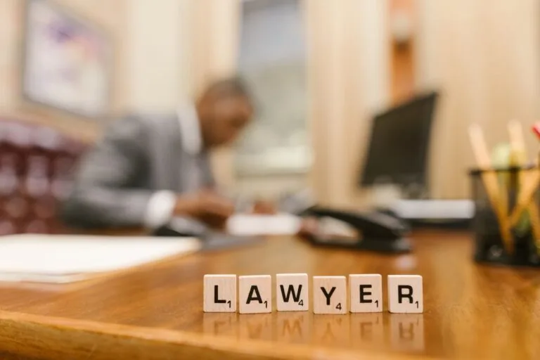 Publicidade na advocacia: o que pode e o que é vedado anunciar 15 Wooden letter tiles spelling LAWYER on a desk, with blurred office setting in the background.