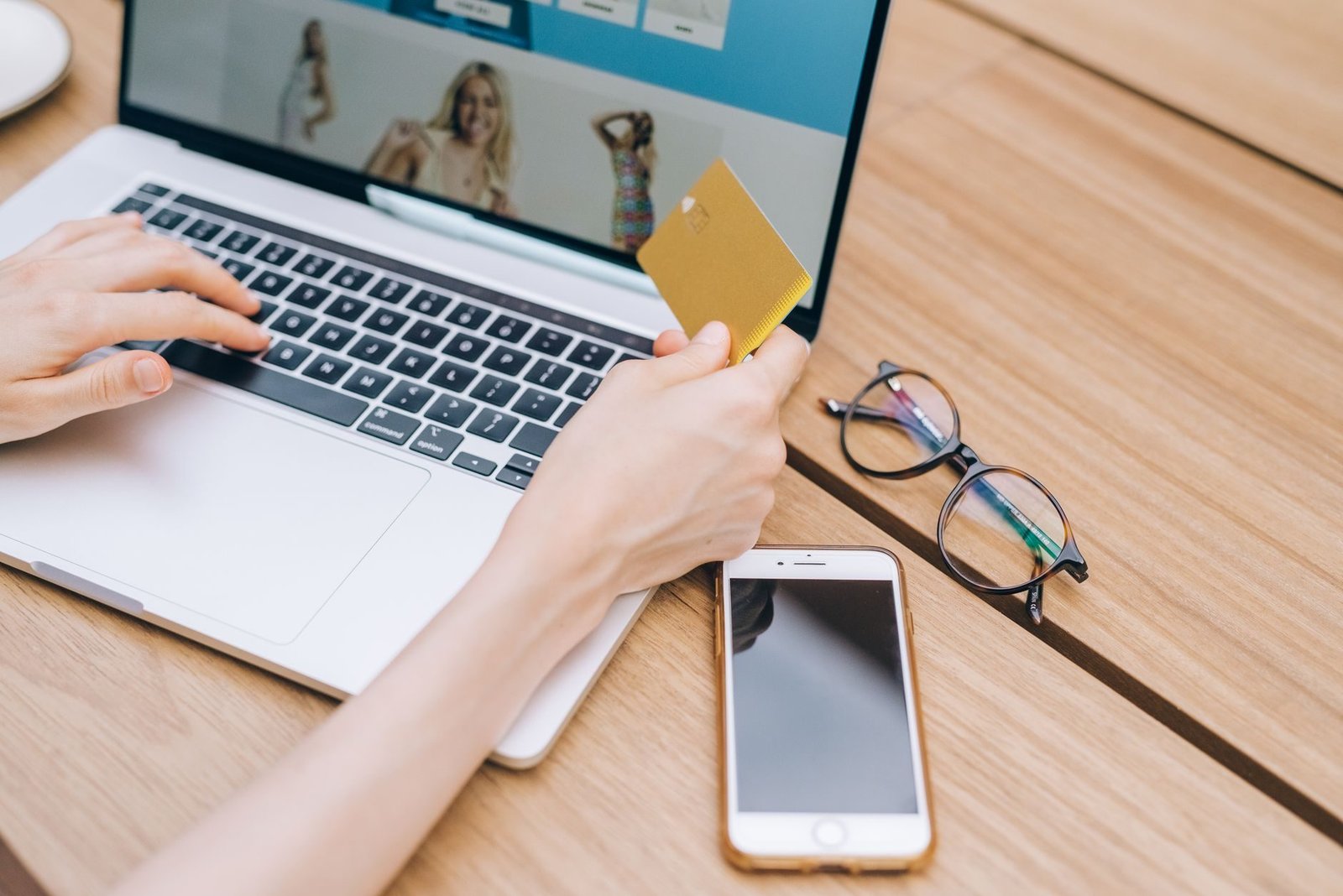 A person makes an online purchase using a credit card on a laptop, with a smartphone and g