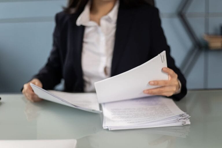 Recurso administrativo: como reverter uma decisão desfavorável sem ir ao Judiciário 15 Businesswoman in formal attire reviewing and organizing documents at an office desk.