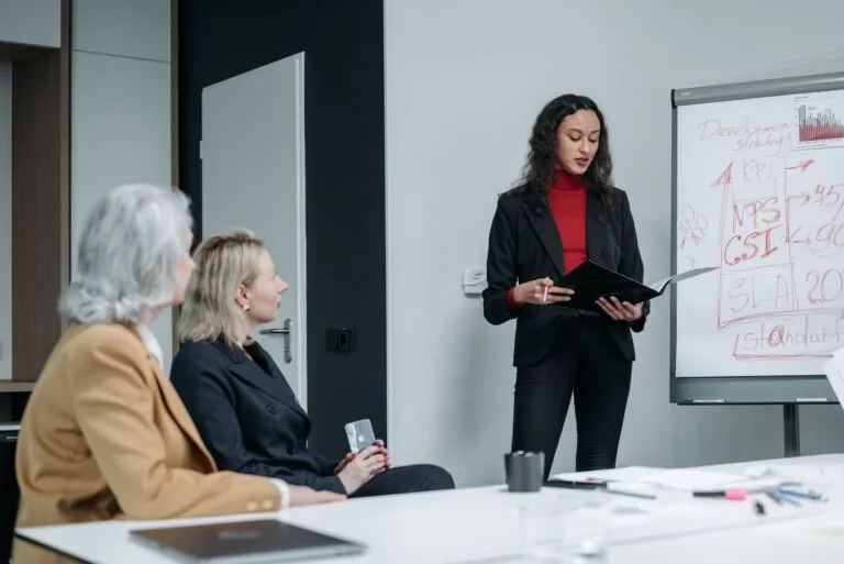 Three business women in a modern office holding a team meeting with presentations and discussions.