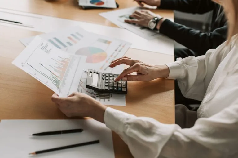 Hands performing financial calculations with charts and a calculator at a meeting table.