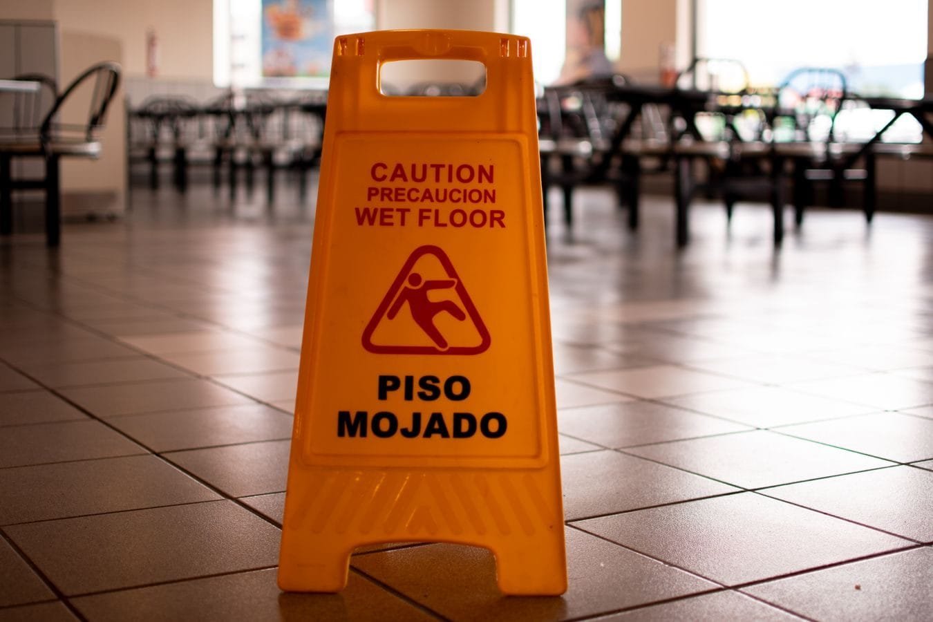 Responsabilidade civil por queda em área comum ou estabelecimento 1 Yellow caution wet floor sign in a cafeteria warns of slippery conditions on tiled floor.