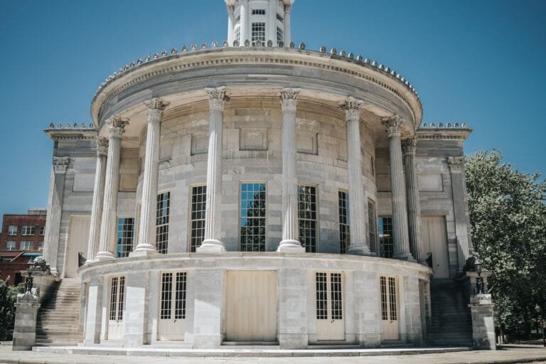 A neoclassical building with columns against a clear blue sky, in an urban town setting.