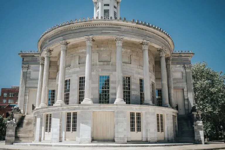 A neoclassical building with columns against a clear blue sky, in an urban town setting.