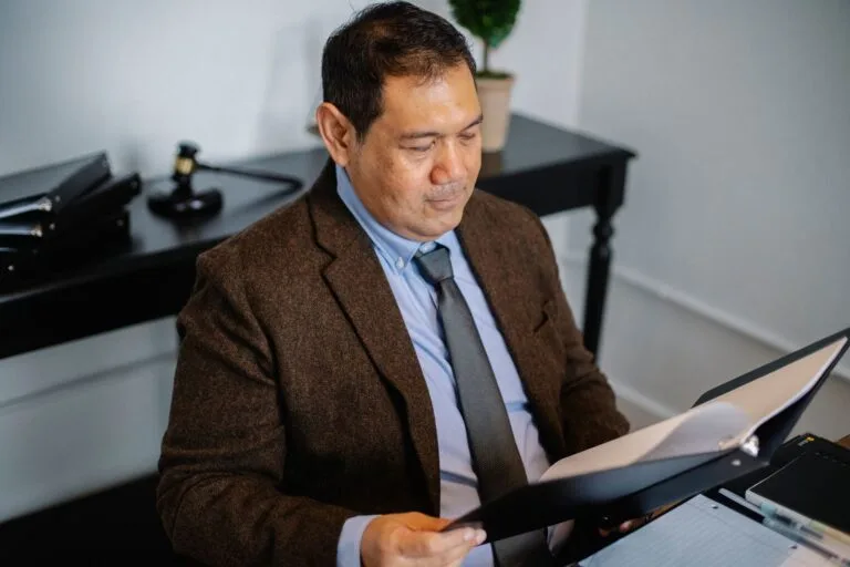 From above of serious ethnic lawyer in elegant suit checking report in folder on blurred b