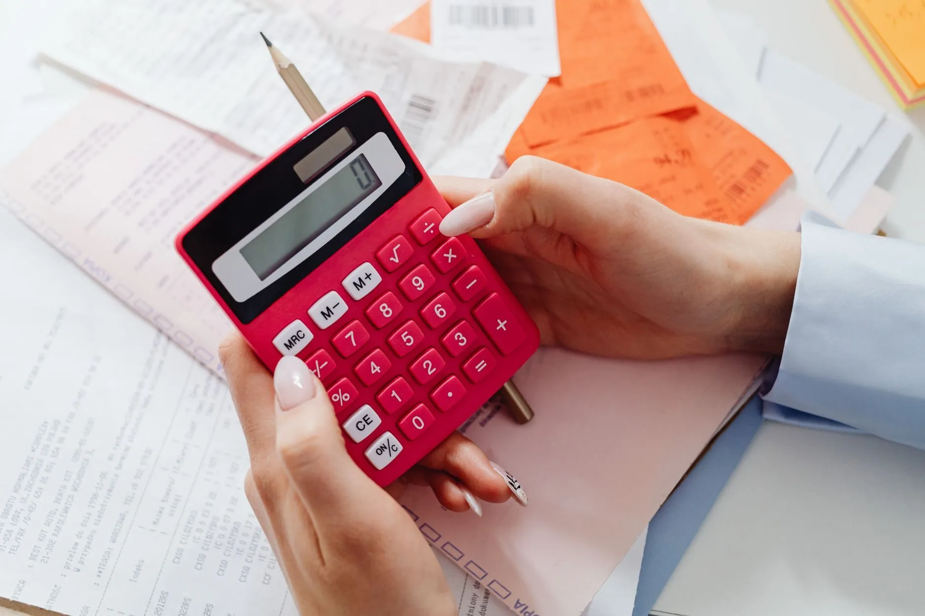 Revisão da vida toda e demais revisões: como avaliar se vale a pena pedir 1 Close-up of hands holding a red calculator, managing finances with documents and receipts.