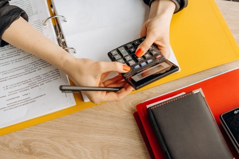 Hands using a calculator at a desk with documents and folders, ideal for finance or accoun