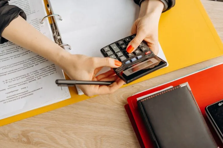 Hands using a calculator at a desk with documents and folders, ideal for finance or accoun