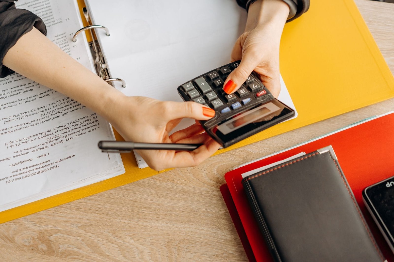 Hands using a calculator at a desk with documents and folders, ideal for finance or accoun