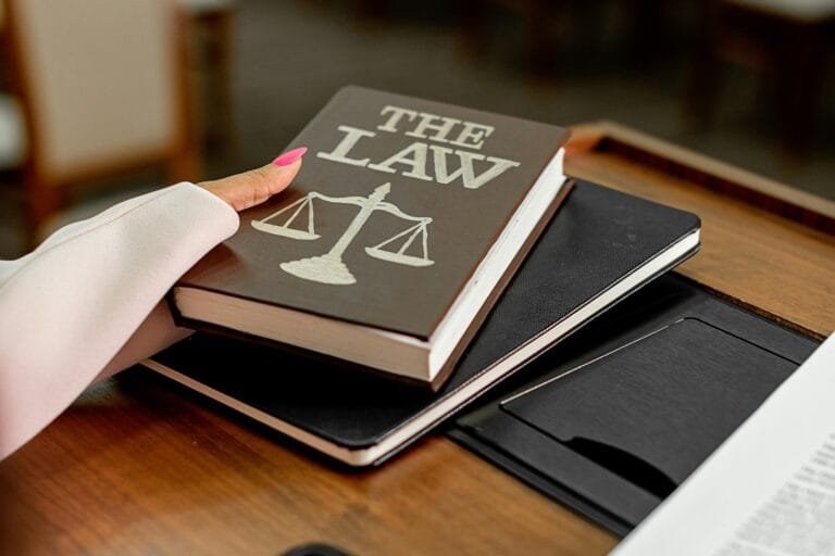 Closeup image of a law book titled The Law on a wooden desk with scales of justice.