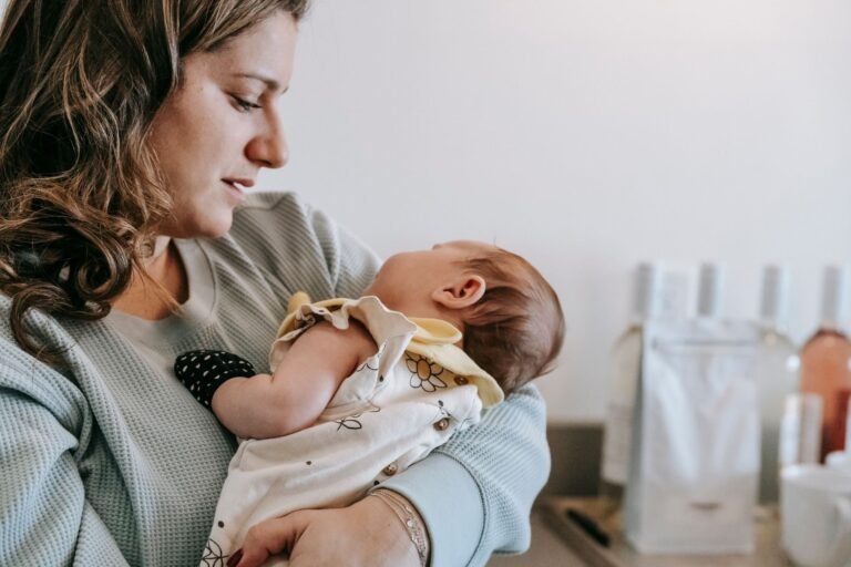 Side view of crop caring mother in casual wear with cute newborn baby in arms standing in 