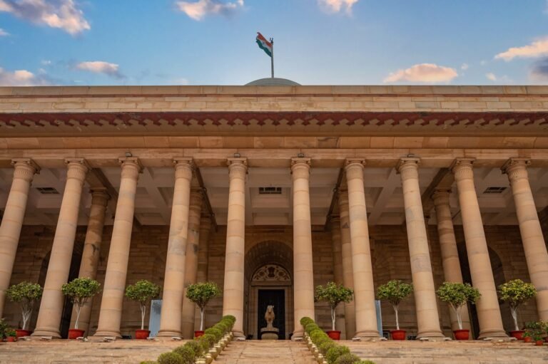 Government building in New Delhi featuring columns and an Indian flag under a vibrant sky.