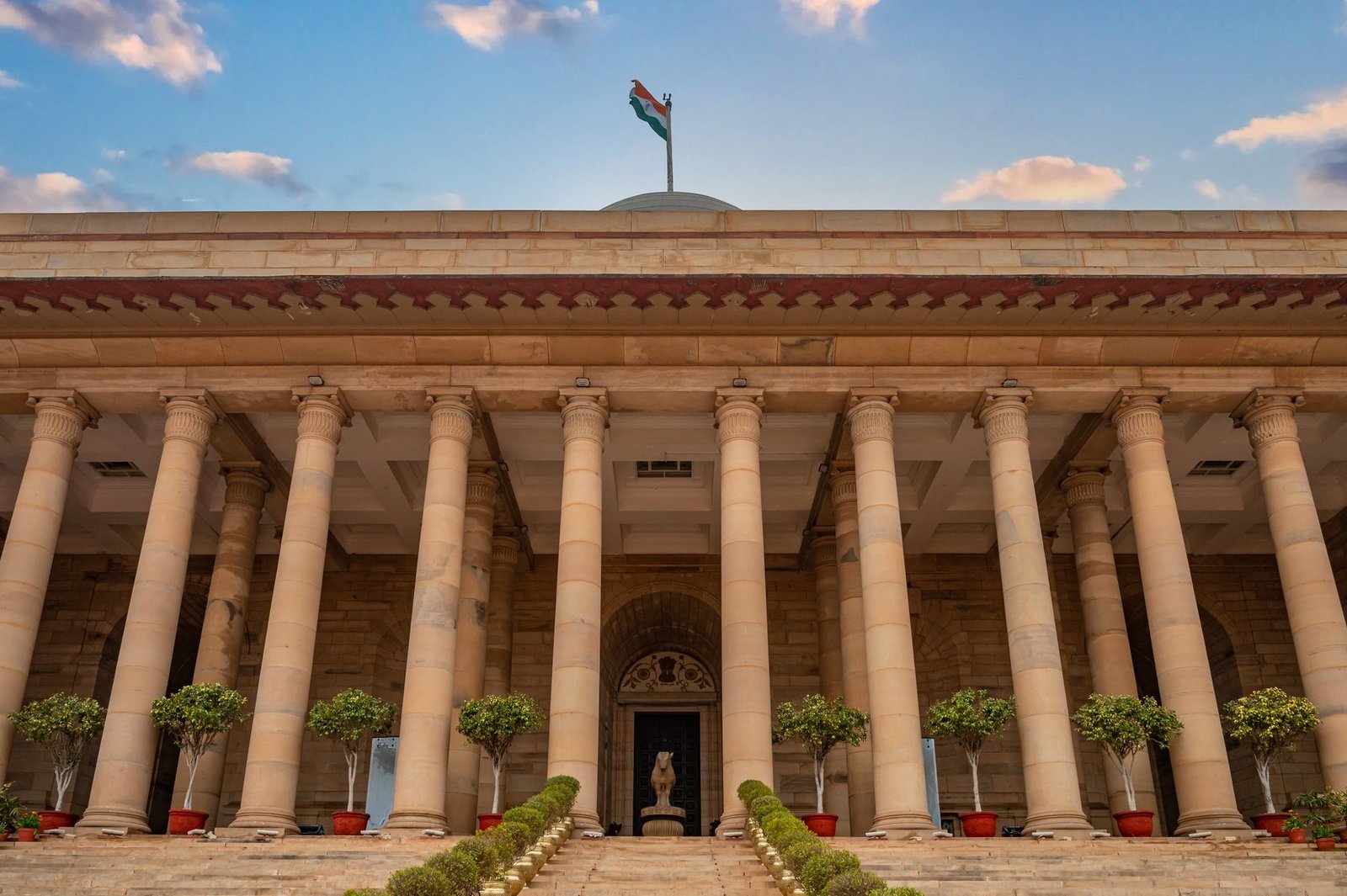 Government building in New Delhi featuring columns and an Indian flag under a vibrant sky.