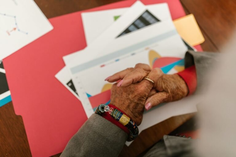 A close-up view of an elderly person's hands with jewelry over business documents and fold