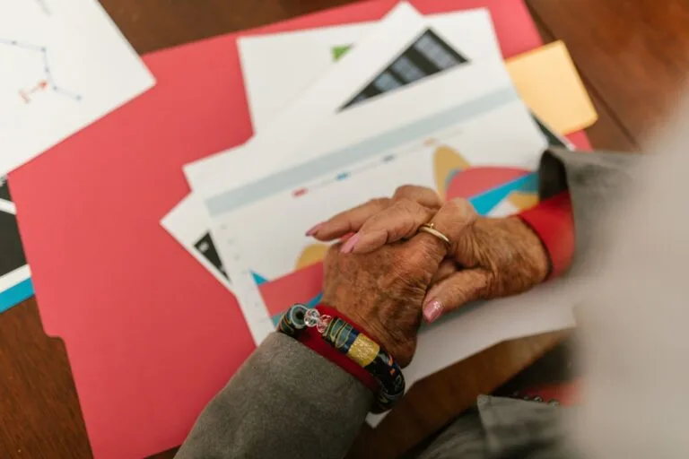 A close-up view of an elderly person's hands with jewelry over business documents and fold