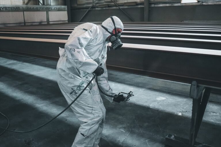 STF declara inconstitucional a idade mínima para aposentadoria especial em atividades insalubres (ADI 6309) 7 Worker in protective gear spray painting metal beams inside a factory setting.