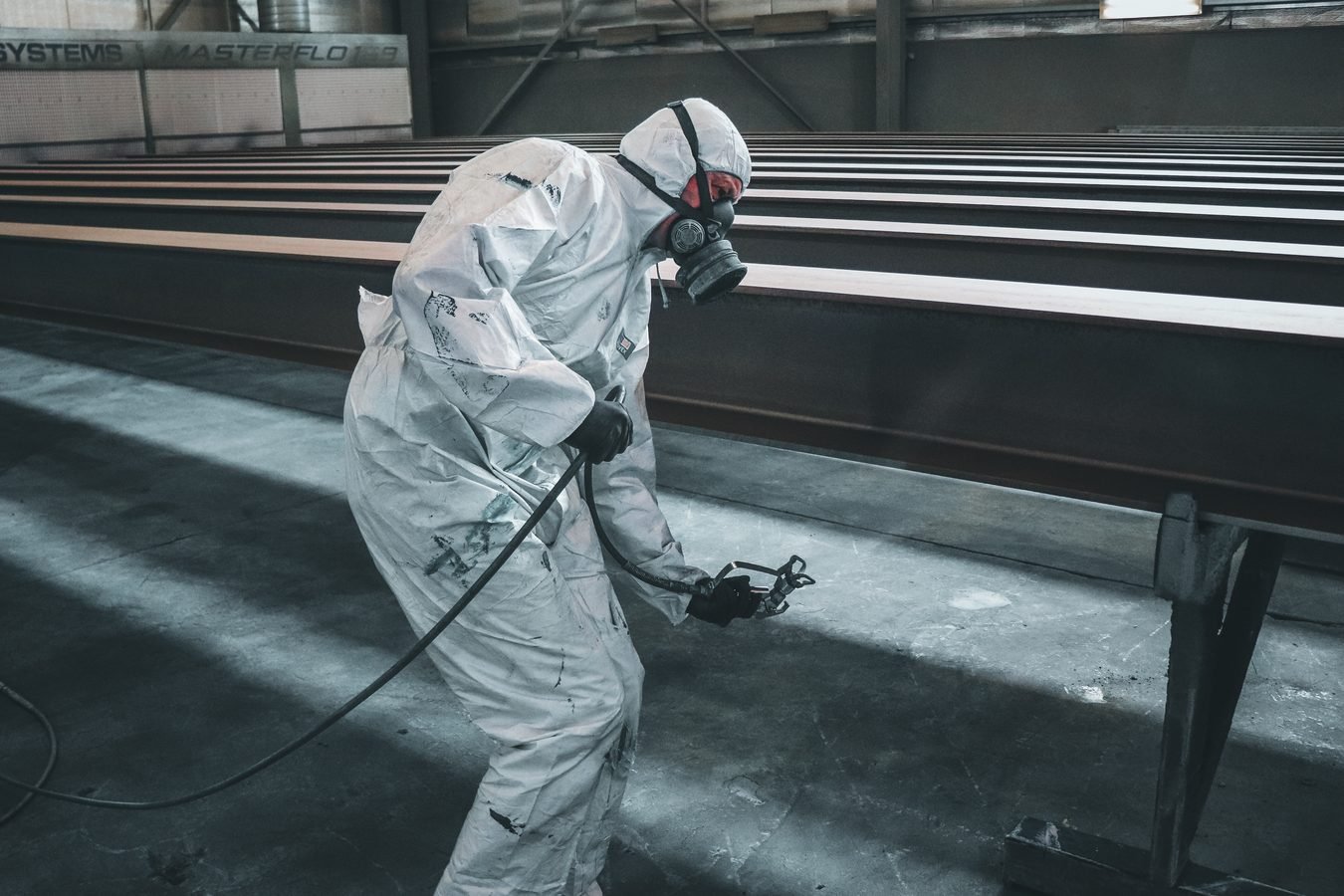 STF declara inconstitucional a idade mínima para aposentadoria especial em atividades insalubres (ADI 6309) 1 Worker in protective gear spray painting metal beams inside a factory setting.