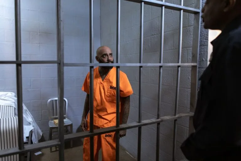STJ afeta ao rito dos repetitivos a retroatividade de pensão por morte e auxílio-reclusão para dependentes menores de 16 anos (Tema 1.421) 2 An inmate in an orange jumpsuit stands behind bars with a guard outside the cell.