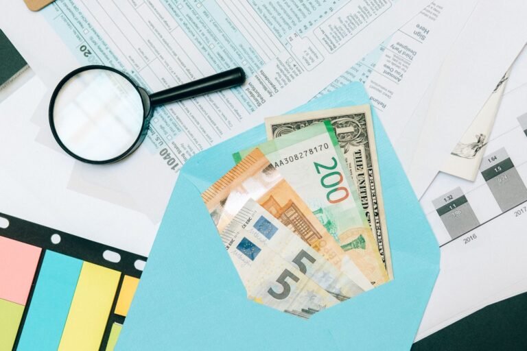 Close-up of tax documents and mixed currency in a blue envelope with a magnifying glass, p