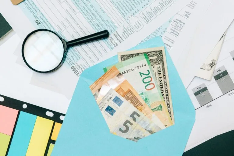 Close-up of tax documents and mixed currency in a blue envelope with a magnifying glass, p