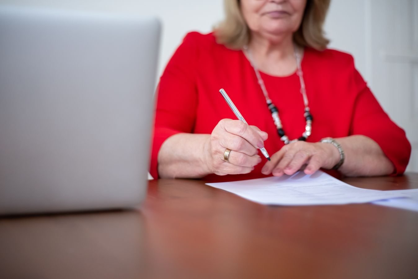 Senior woman writing on paper with a pen, working on documents at a desk.