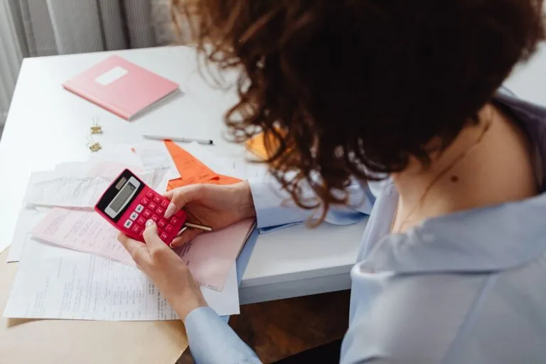 Woman calculating expenses with documents and calculator at work desk.