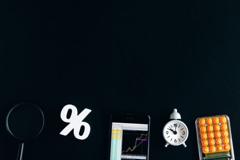 Flat lay of financial analysis tools including phone, clock, and calculator on black backg