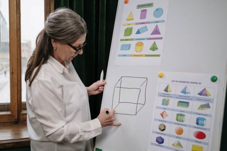 Senior woman instructing a geometry lesson using a whiteboard with 3D shapes.