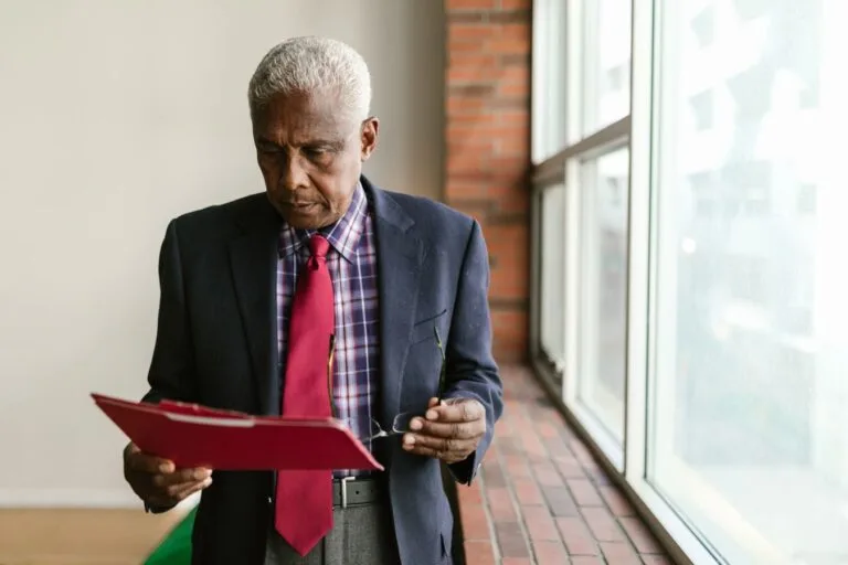 TNU firma tese sobre prescrição na revisão de aposentadoria de servidores públicos por reconhecimento de tempo especial estatutário 7 Elderly man in formal attire reviewing documents indoors with natural light.