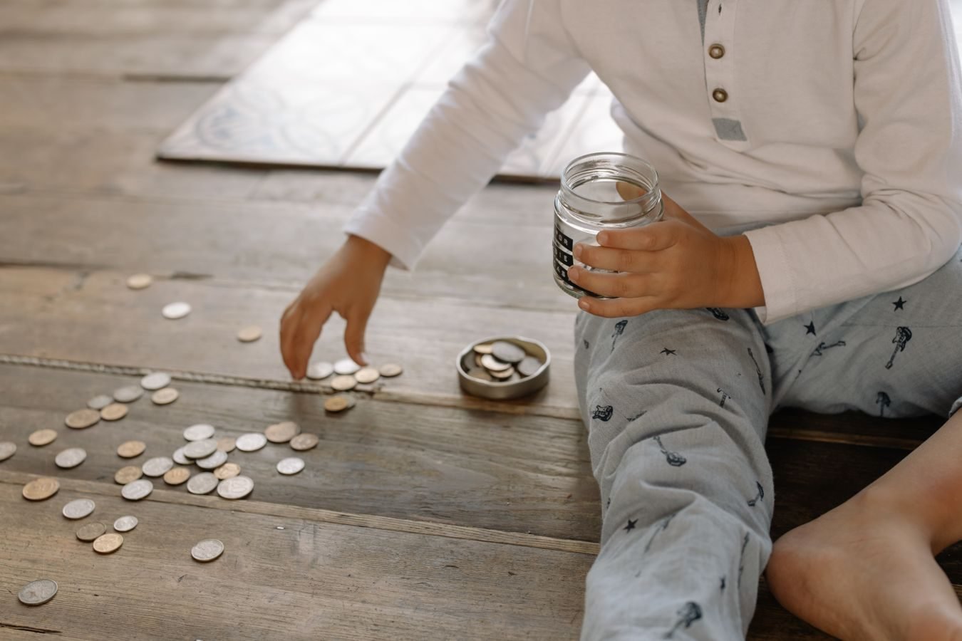 TNU fixa Tema 369 e determina que benefício previdenciário superior ao salário-mínimo entra integralmente no cálculo da renda per capita do BPC/LOAS 1 A young child collects coins into a jar on a wooden floor, symbolizing savings.