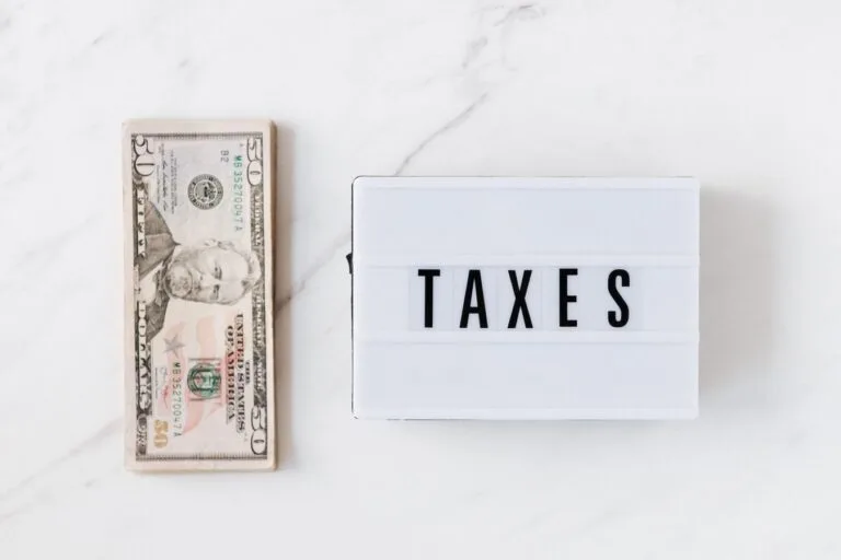 Transação tributária: como negociar dívidas com a Fazenda e obter descontos 6 Top view composition of stack of American dollars placed on white marble surface with white retro light box with TAXES i