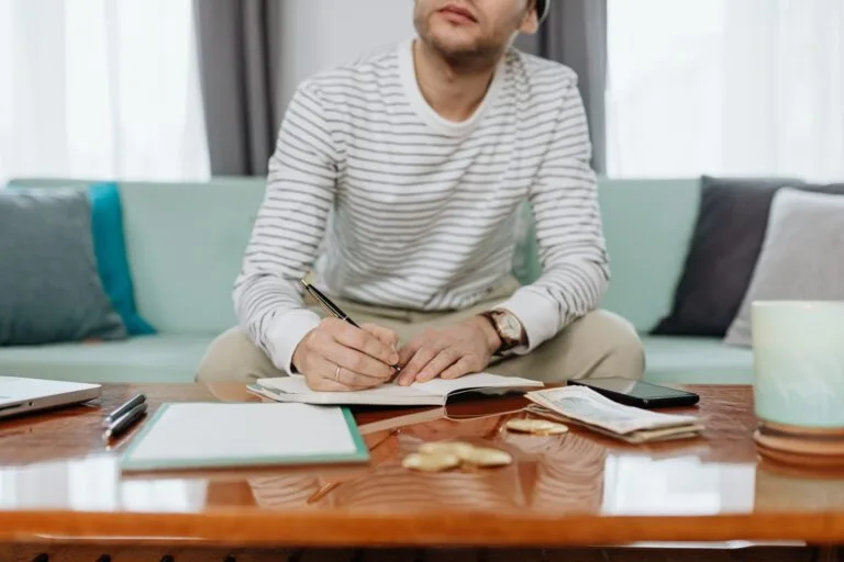Tributação do Autônomo: Carnê-Leão e Deduções 6 A man sits at a table writing in a notebook, managing finances and budgeting.