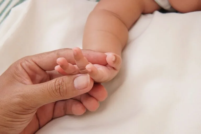 Close-up of a parent's hand gently holding a baby's hand, symbolizing love and care.