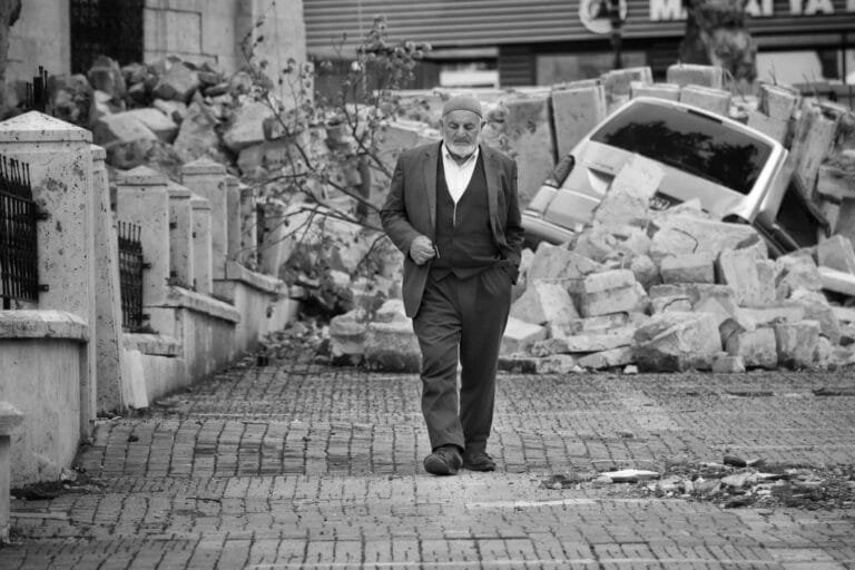 Elderly man walks through rubble after an earthquake, conveying resilience amidst destruction.