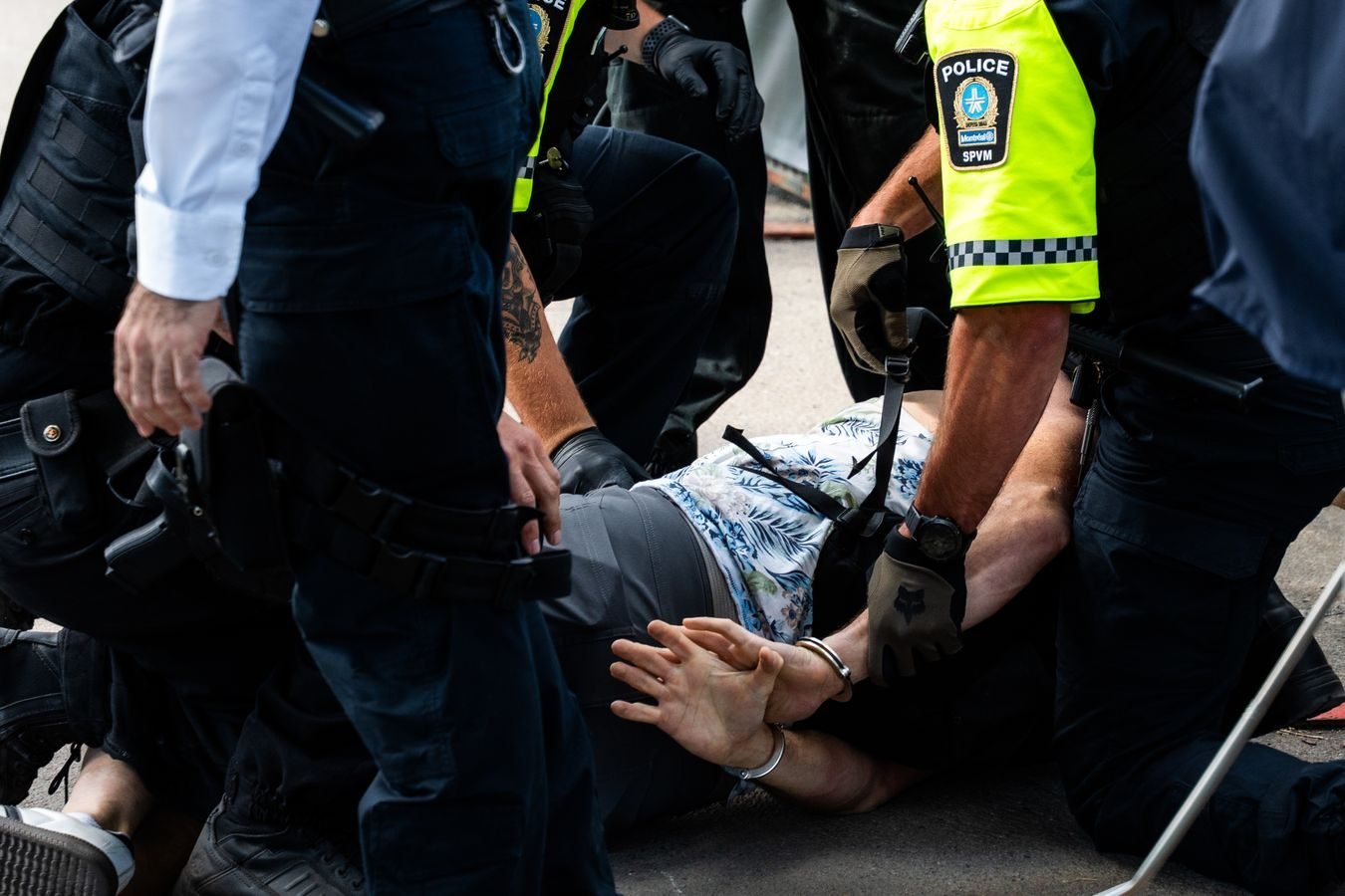 Operação Sem Desconto: PF deflagra nova fase com 66 mandados em oito estados e bloqueio de R$ 400 milhões contra fraudes no INSS 1 Multiple police officers detain a person on a city street, using handcuffs to restrain them.