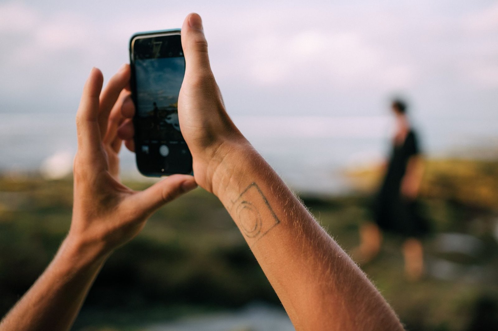 Uso da imagem de funcionarios e clientes: o que a empresa pode publicar 1 Person taking photo with smartphone at beach capturing another in the distance.