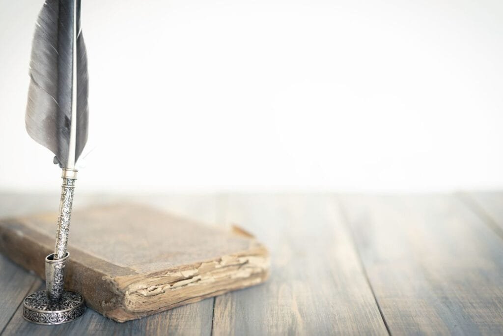 A detailed feather quill beside an aged book on a wooden surface, evoking a classic atmosphere.