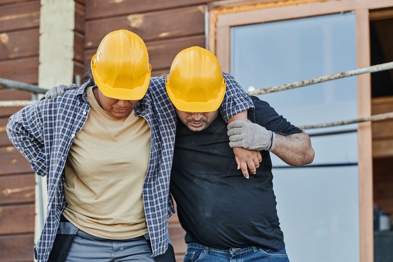 Acidente de Trabalho e Benefícios do INSS: Guia Completo 1 Two construction workers in hard hats assisting each other at a building site, highlighting teamwork.
