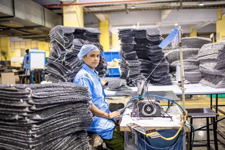 Female factory worker operating sewing machine in textile production area, focusing on eff
