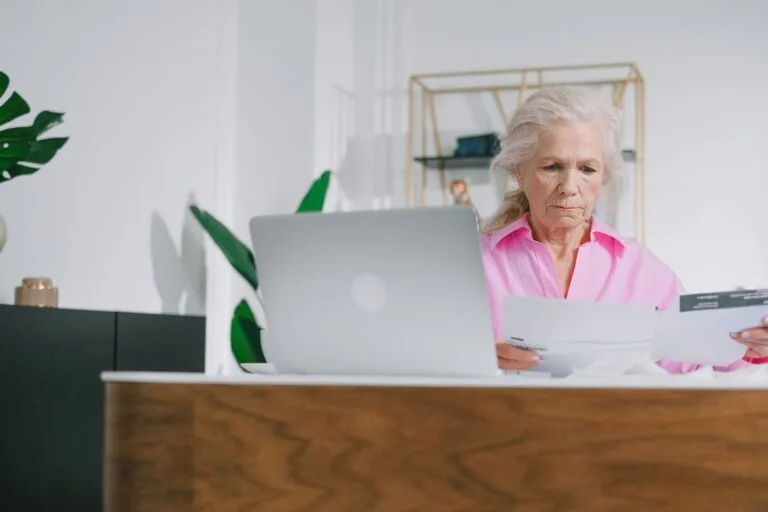 Acumulação de Benefícios Previdenciários: Regras da EC 103/2019 3 Elderly woman focused on paperwork at home office with laptop.