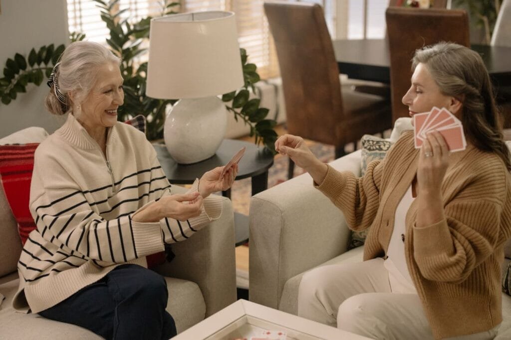 Recebo um benefício e queria saber se posso acumular com outro. 1 Two senior women playing cards and enjoying leisure time in a cozy living room.