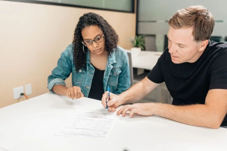 A couple working together to sign important legal documents at a desk in an office setting