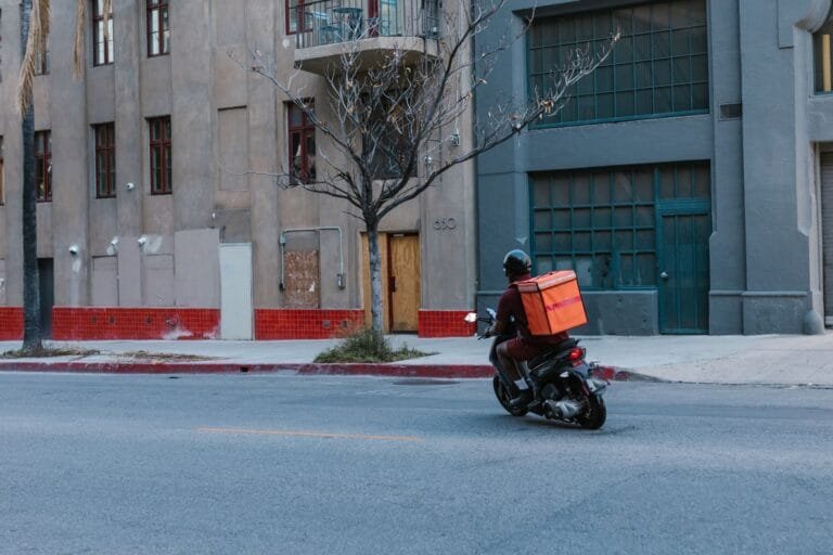 Adicional de Periculosidade Motociclista Dispensa Regulamentação 4 Street view of a courier on a motorcycle delivering in an urban setting.