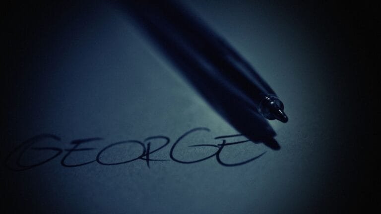 Resultados 11 Artistic close-up of a pen casting shadow on handwritten name George in soft dark lighting.