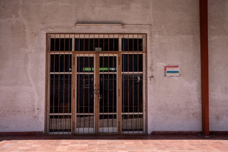 A rustic iron gate in a textured wall with a warning sign, captured in bright daylight.