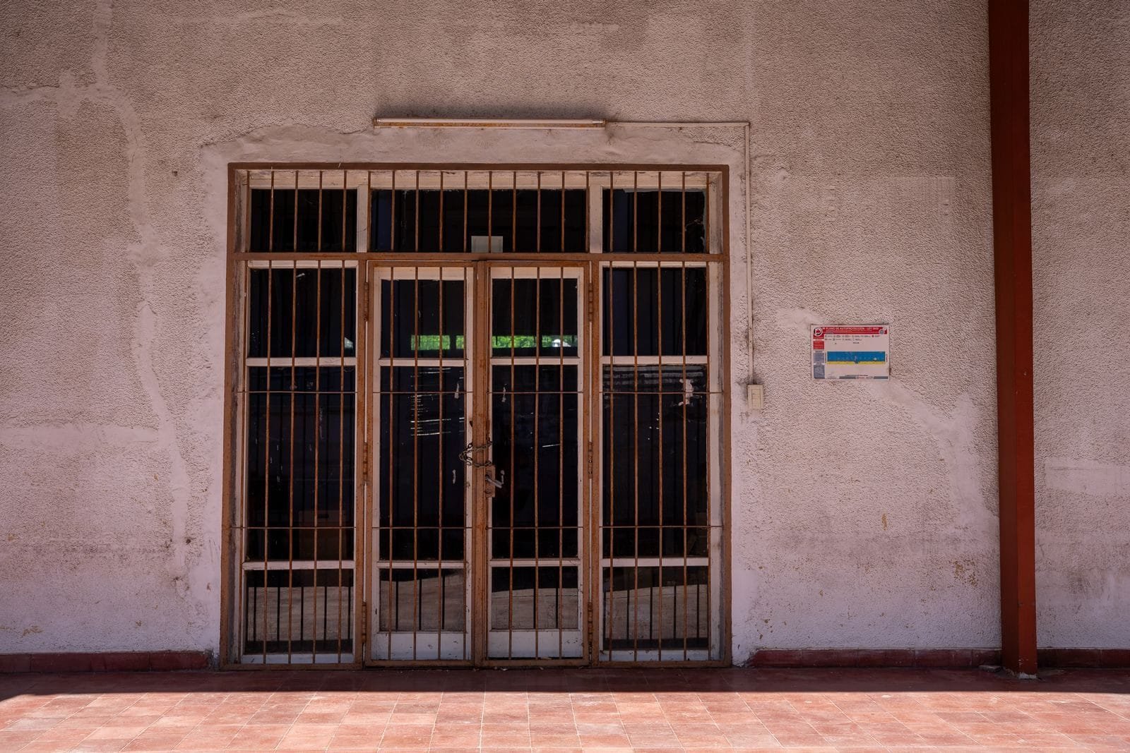 A rustic iron gate in a textured wall with a warning sign, captured in bright daylight.